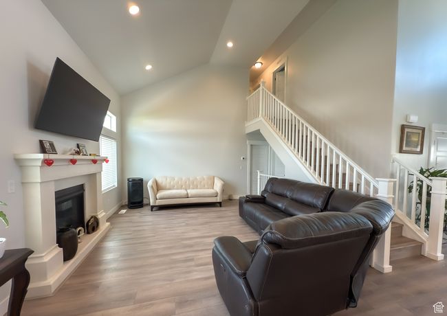 Living room featuring wood finished floors, a glass covered fireplace, stairs, lofted ceiling, and recessed lighting | Image 6