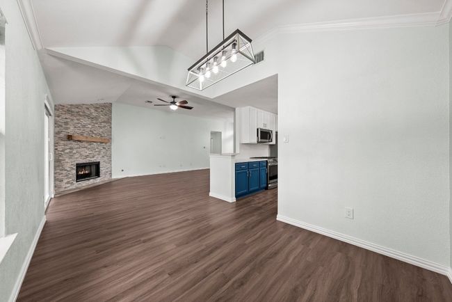 Unfurnished living room featuring ceiling fan, dark wood-style flooring, a stone fireplace, baseboards, and high vaulted ceiling | Image 7