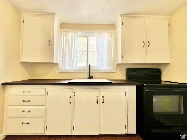 Kitchen featuring dark countertops, white cabinetry, black electric range oven, and a sink | Image 16