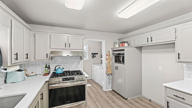 Kitchen featuring stainless steel gas range oven, washer and clothes dryer, under cabinet range hood, light wood-style flooring, and decorative backsplash | Image 31