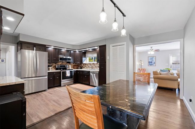 Kitchen with hanging light fixtures, stainless steel appliances, dark brown cabinets, light wood-type flooring, and backsplash | Image 11