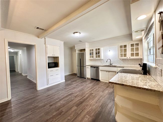 Kitchen with stainless steel appliances, ornamental molding, decorative backsplash, light stone countertops, and dark wood-style floors | Image 14