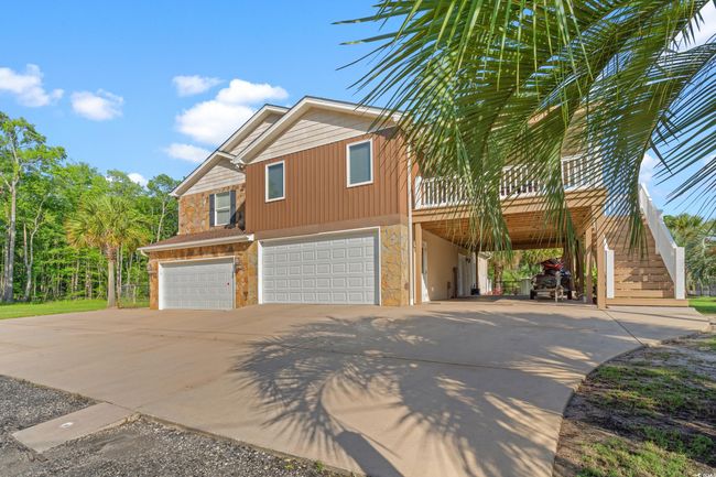 View of side of property featuring stone siding, concrete driveway, a garage, and stairway | Image 37