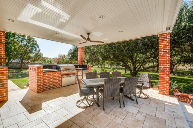 View of patio featuring an outdoor kitchen, outdoor dining area, a grill, fence, and a ceiling fan | Image 32