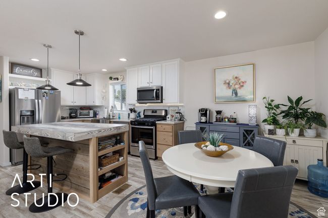 Kitchen featuring stainless steel appliances, open shelves, a breakfast bar area, white cabinets, and light stone countertops | Image 9