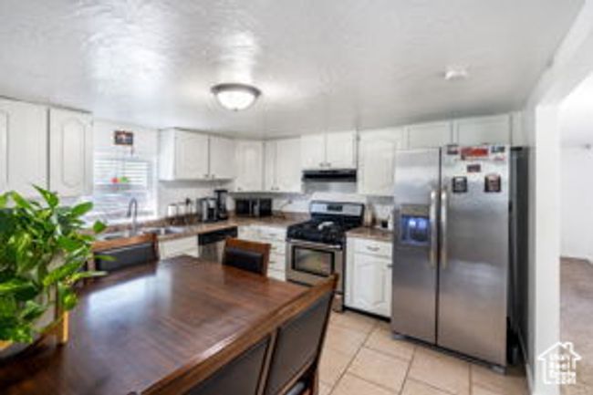 Kitchen with under cabinet range hood, appliances with stainless steel finishes, white cabinets, a sink, and light tile patterned flooring | Image 10