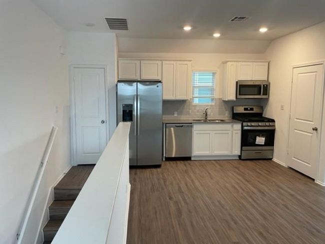 Kitchen with stainless steel appliances, a sink, white cabinetry, backsplash, and dark wood-style floors | Image 7