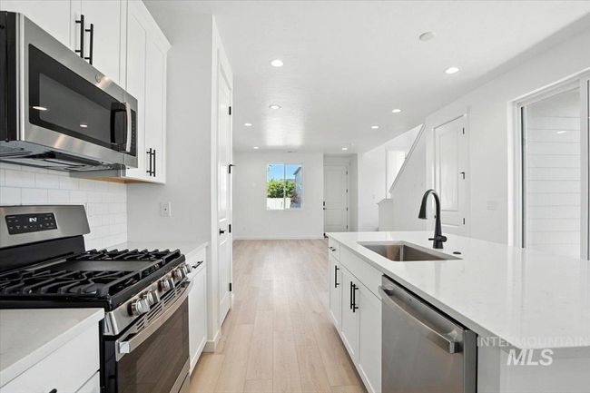 Kitchen with stainless steel appliances, light wood finished floors, a kitchen island with sink, recessed lighting, and backsplash | Image 11
