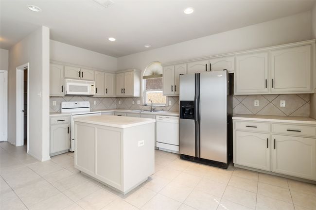 Kitchen with white appliances, a kitchen island, a sink, decorative backsplash, and light countertops | Image 21