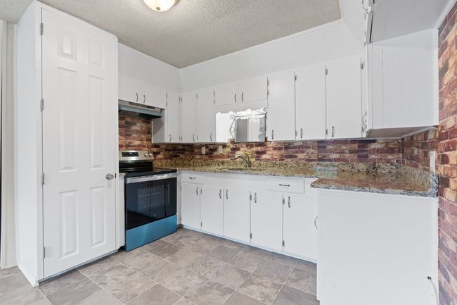 Kitchen with stainless steel electric stove, under cabinet range hood, a textured ceiling, tasteful backsplash, and white cabinets | Image 7