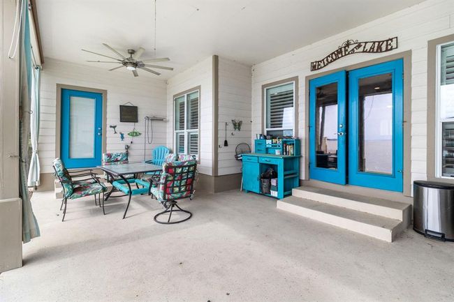 This inviting patio features a spacious seating area with colorful chairs and a glass table. It's accented by bright blue doors and trim, a ceiling fan, and a wall-mounted decor piece. Ideal for relaxing or entertaining. | Image 26