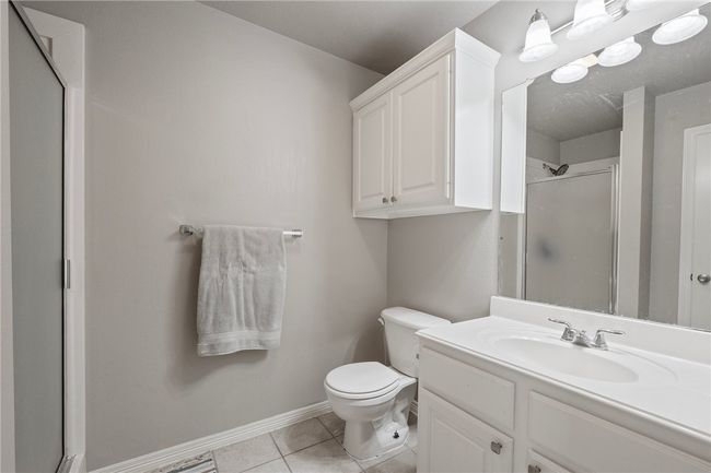 Bathroom with toilet, a shower with shower door, vanity, tile patterned flooring, and baseboards | Image 11