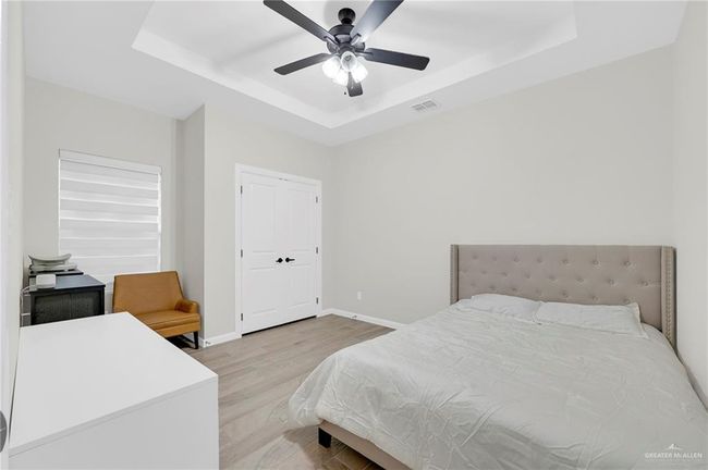 Bedroom with light wood-style tile flooring, ceiling fan, baseboards, visible vents, and a tray ceiling | Image 15