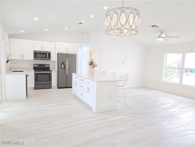 Kitchen featuring appliances with stainless steel finishes, vaulted ceiling, a breakfast bar area, a sink, and light countertops | Image 7
