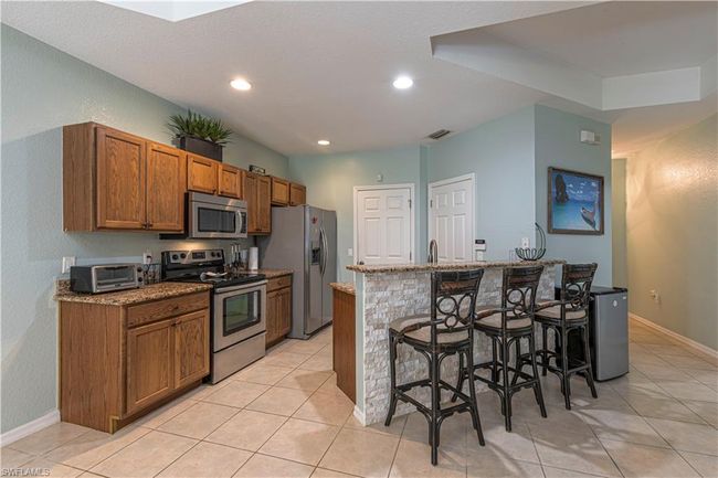 Kitchen featuring a kitchen bar, visible vents, light tile patterned flooring, stainless steel appliances, and brown cabinets | Image 10