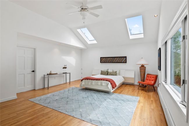 Bedroom featuring a skylight, light wood-type flooring, high vaulted ceiling, and ceiling fan | Image 18