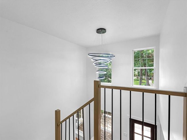 This photo showcases a bright, airy stairwell with a modern spiral chandelier. Large windows provide natural light and views of greenery. The design features a sleek railing and a welcoming entrance below. | Image 33