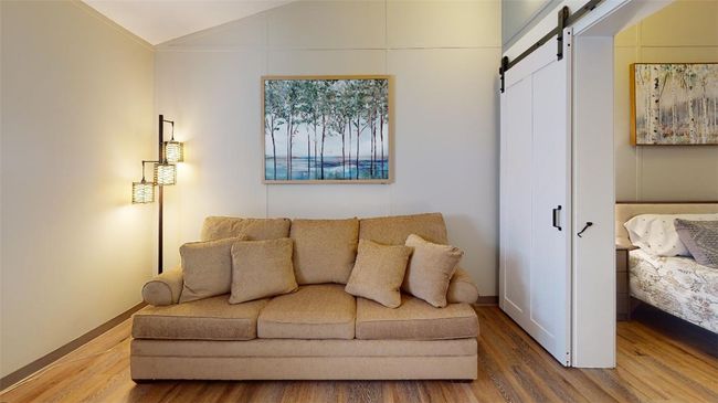 Living area featuring wood finished floors, a barn door, lofted ceiling, and baseboards | Image 43