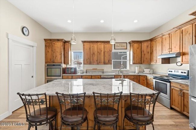 Kitchen featuring stainless steel appliances, brown cabinets, under cabinet range hood, light wood-style floors, and recessed lighting | Image 8