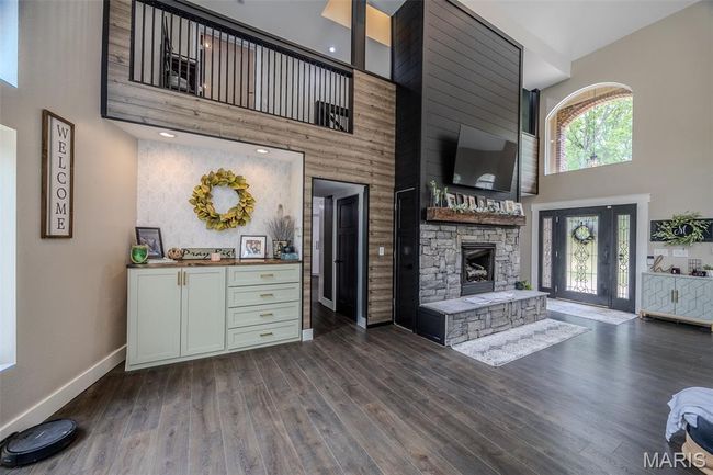 Living room featuring a high ceiling, a stone fireplace, and dark wood-type flooring | Image 12