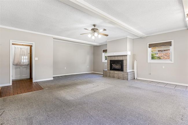 Unfurnished living room featuring a textured ceiling, carpet, baseboards, a fireplace, and ceiling fan | Image 42
