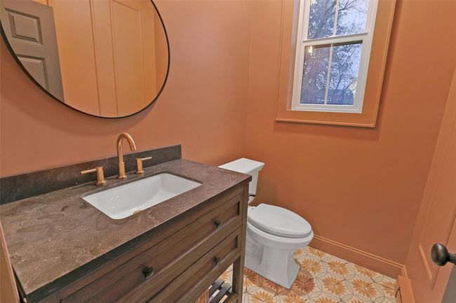 Powder room includes rustic wood vanity, granite top, bronze fixtures, porcelain floor tile and Kohler comfort height toilet. | Image 21
