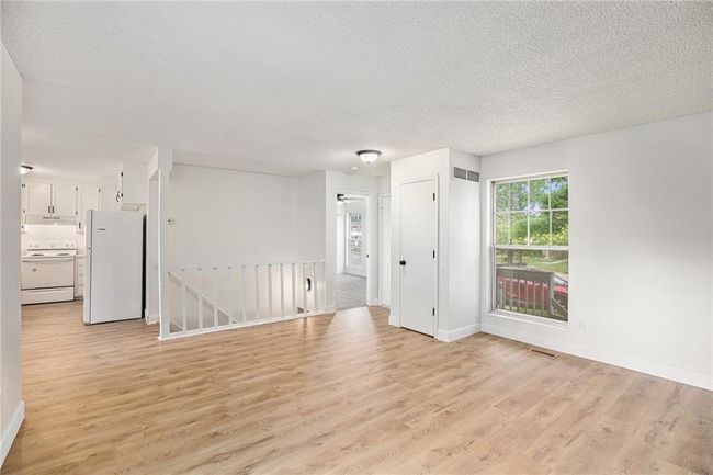 Empty room with light wood-style floors, a textured ceiling, and baseboards | Image 5