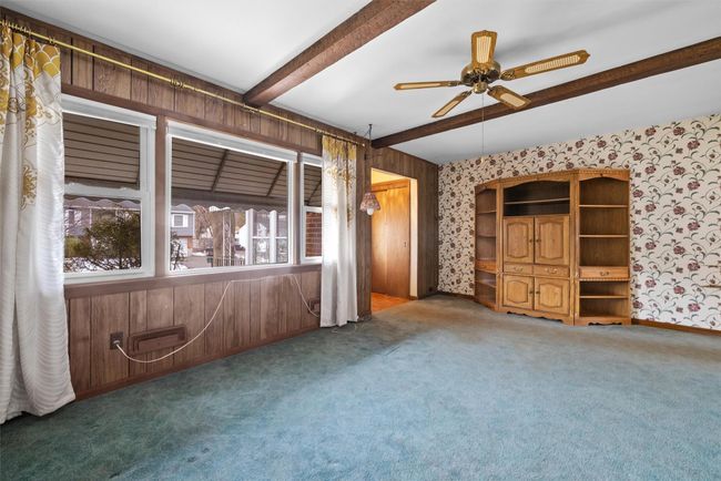 Empty room featuring a ceiling fan, dark carpet, beam ceiling, and wallpapered walls | Image 9