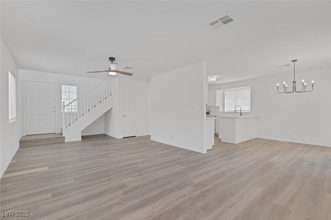 Unfurnished living room featuring a chandelier, light wood-style flooring, ceiling fan, and stairs | Image 6