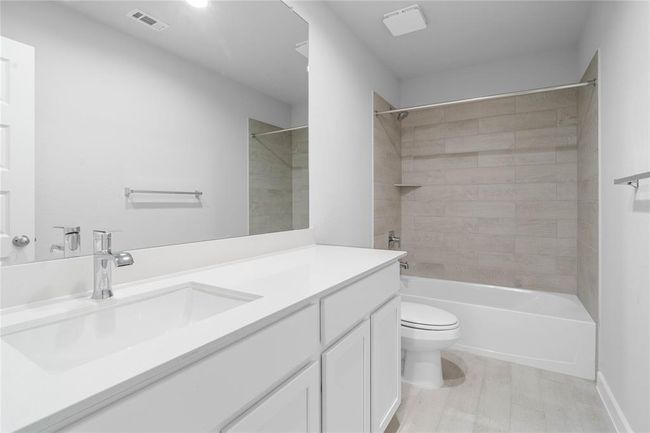 Secondary bath features tile flooring, bath/shower combo with tile surround, stained wood cabinets, beautiful light countertops, mirror, sleek fixtures, and modern finishes. | Image 17