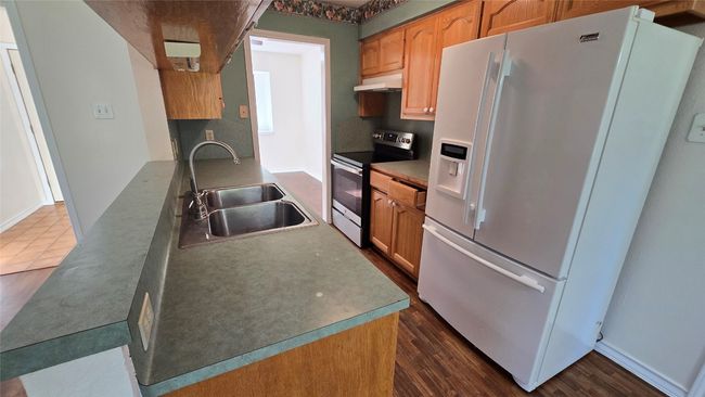 Kitchen featuring white refrigerator with ice dispenser, stainless steel range with electric cooktop, under cabinet range hood, and dark wood-style floors | Image 13