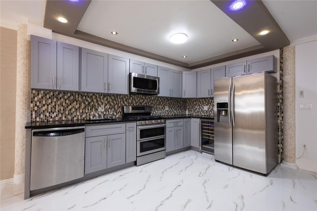 Kitchen with a tray ceiling, tasteful backsplash, gray cabinetry, beverage cooler, and appliances with stainless steel finishes | Image 7