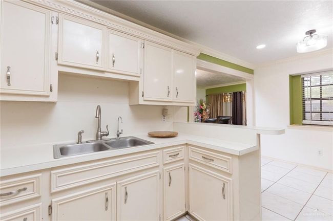 Kitchen featuring ornamental molding, a sink, a peninsula, light countertops, and light tile patterned floors | Image 5