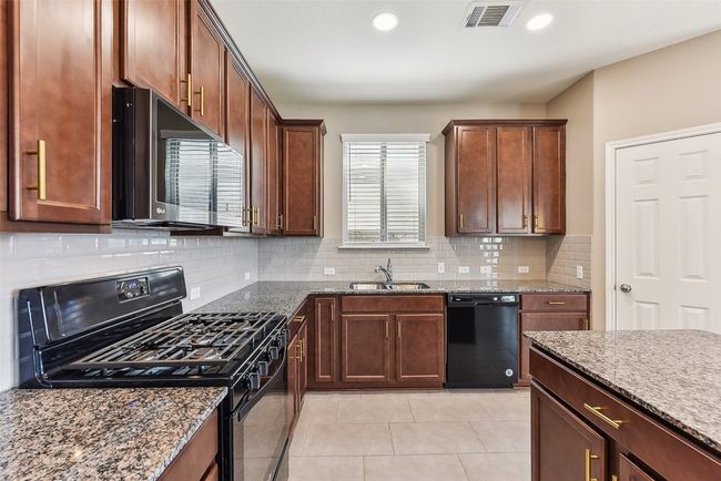 Kitchen with a sink, visible vents, black appliances, and dark stone counters | Image 7