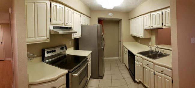 Kitchen has stainless steel appliances, pantry and stacked washer and dryers in the utility space. Ceramic tile floors. | Image 4