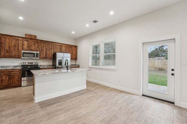 Kitchen with visible vents, a center island with sink, wood plank tile floor, stainless steel appliances, and light stone countertops | Image 13