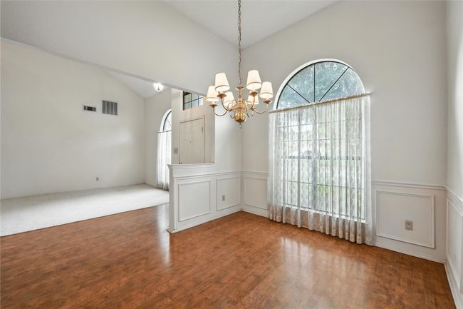 Empty room featuring a chandelier, a decorative wall, a wainscoted wall, wood finished floors, and high vaulted ceiling | Image 4