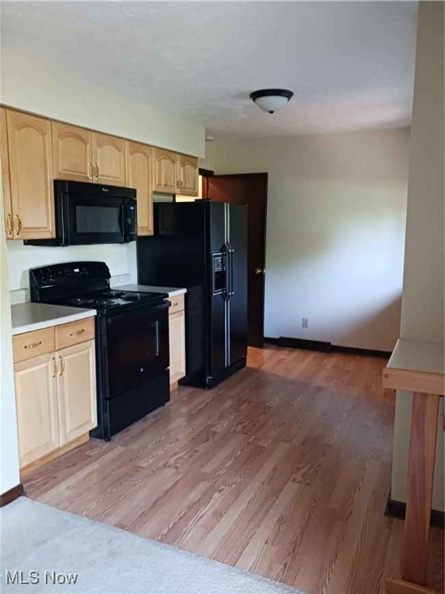 Kitchen with stove, light wood-style flooring, light brown cabinetry, black fridge, and light countertops | Image 4