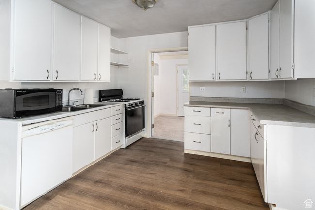 Kitchen with white dishwasher, range with gas cooktop, black microwave, dark wood-type flooring, and white cabinets | Image 17