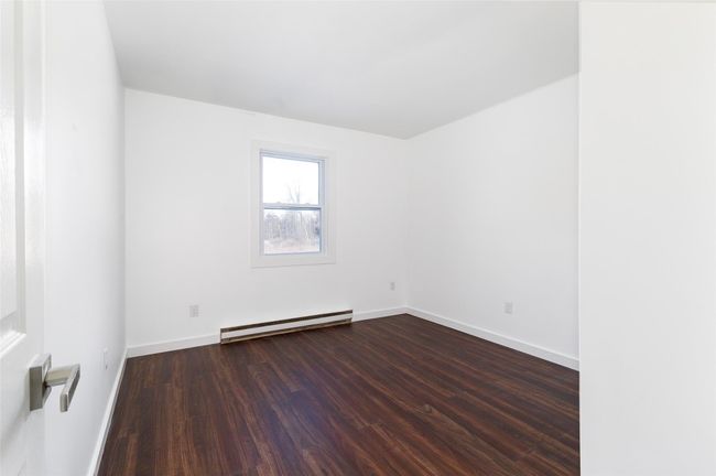 Unfurnished bed room with a baseboard radiator, baseboards, and dark wood-type flooring | Image 8