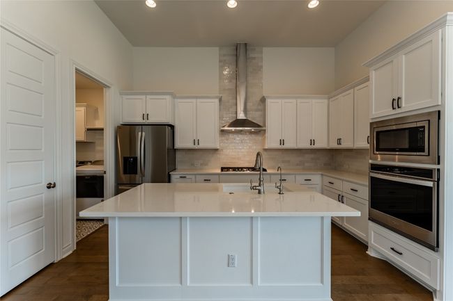 Kitchen with appliances with stainless steel finishes, wall chimney range hood, white cabinets, tasteful backsplash, and light countertops | Image 13