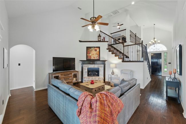 Living room with high vaulted ceiling, a ceiling fan, arched walkways, dark wood-style floors, and stairway | Image 17
