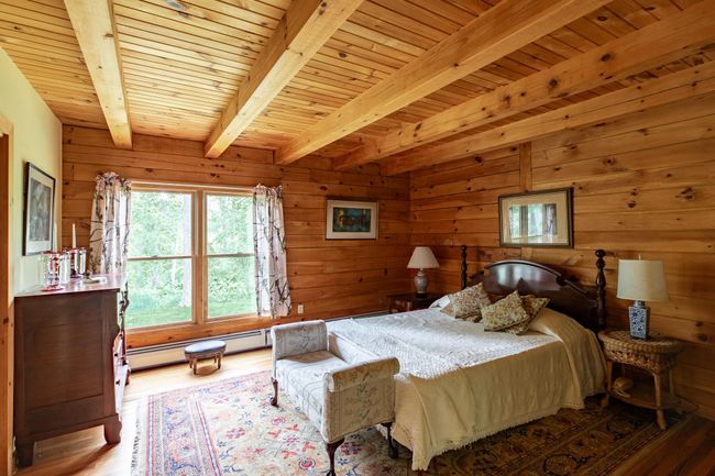 Bedroom with wood finished floors, wood ceiling with exposed beams, a baseboard heating unit, and wooden walls | Image 12