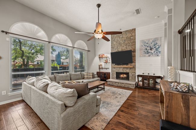 Living area with a textured ceiling, a fireplace, dark wood-style floors, wood walls, and a ceiling fan | Image 9