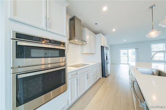 Kitchen with appliances with stainless steel finishes, wall chimney exhaust hood, a sink, white cabinetry, and recessed lighting | Image 16