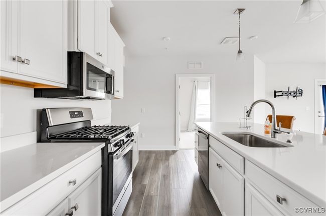 Kitchen featuring stainless steel appliances, dark wood-type flooring, light countertops, and white cabinetry | Image 4