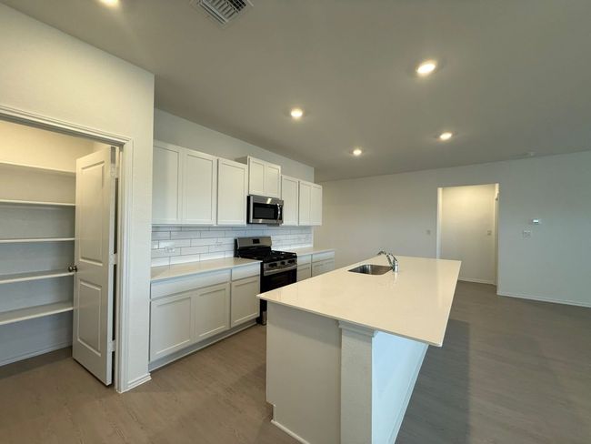 Kitchen with appliances with stainless steel finishes, a sink, wood finished floors, backsplash, and a center island with sink | Image 19