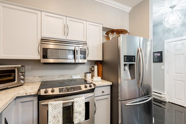 Kitchen featuring light stone counters, a toaster, stainless steel appliances, white cabinets, and crown molding | Image 6
