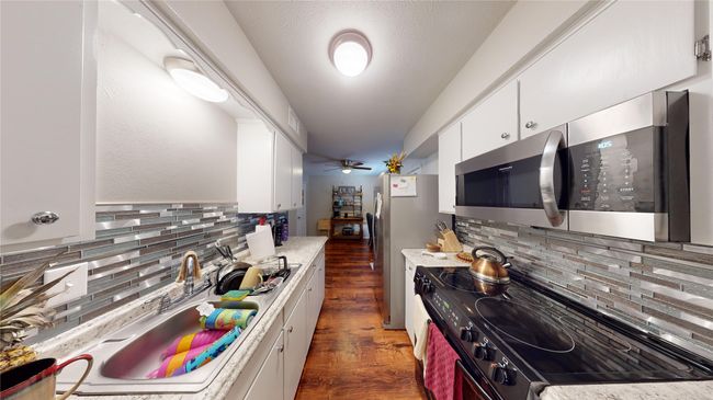 Kitchen featuring white cabinets, light countertops, stainless steel appliances, dark wood-type flooring, and backsplash | Image 7