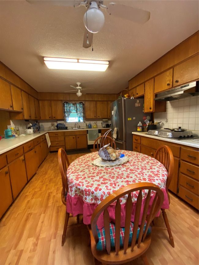 Kitchen with range hood, fridge, stovetop, brown cabinets, and a textured ceiling | Image 6